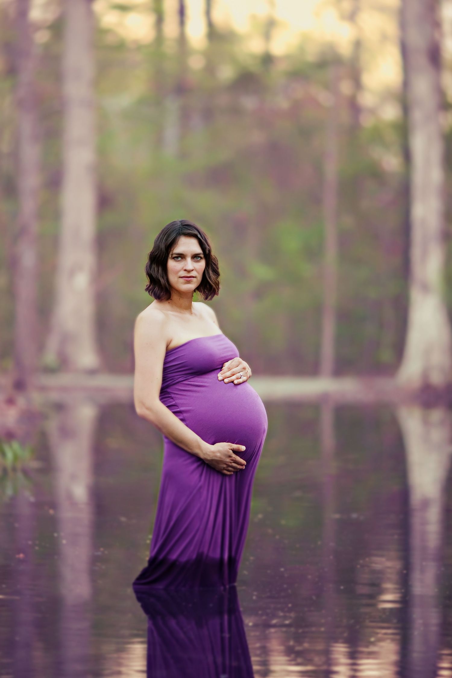 Maternity portrait in purple dress standing in reflective flooded forest.