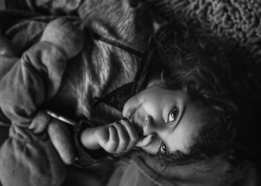 Dramatic black and white portrait of a child with curly hair lying down.