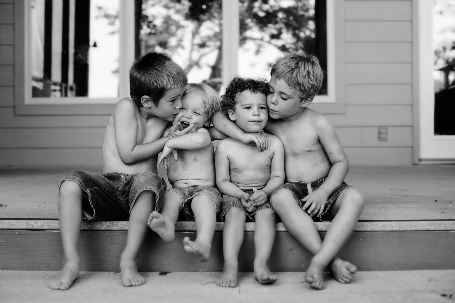 Black and white photo of four children sitting together on a porch.