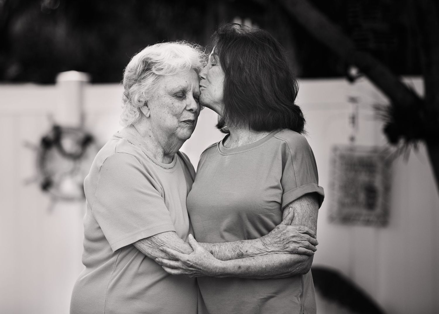 Two elderly women share an intimate embrace while smiling warmly at each other in black and white.