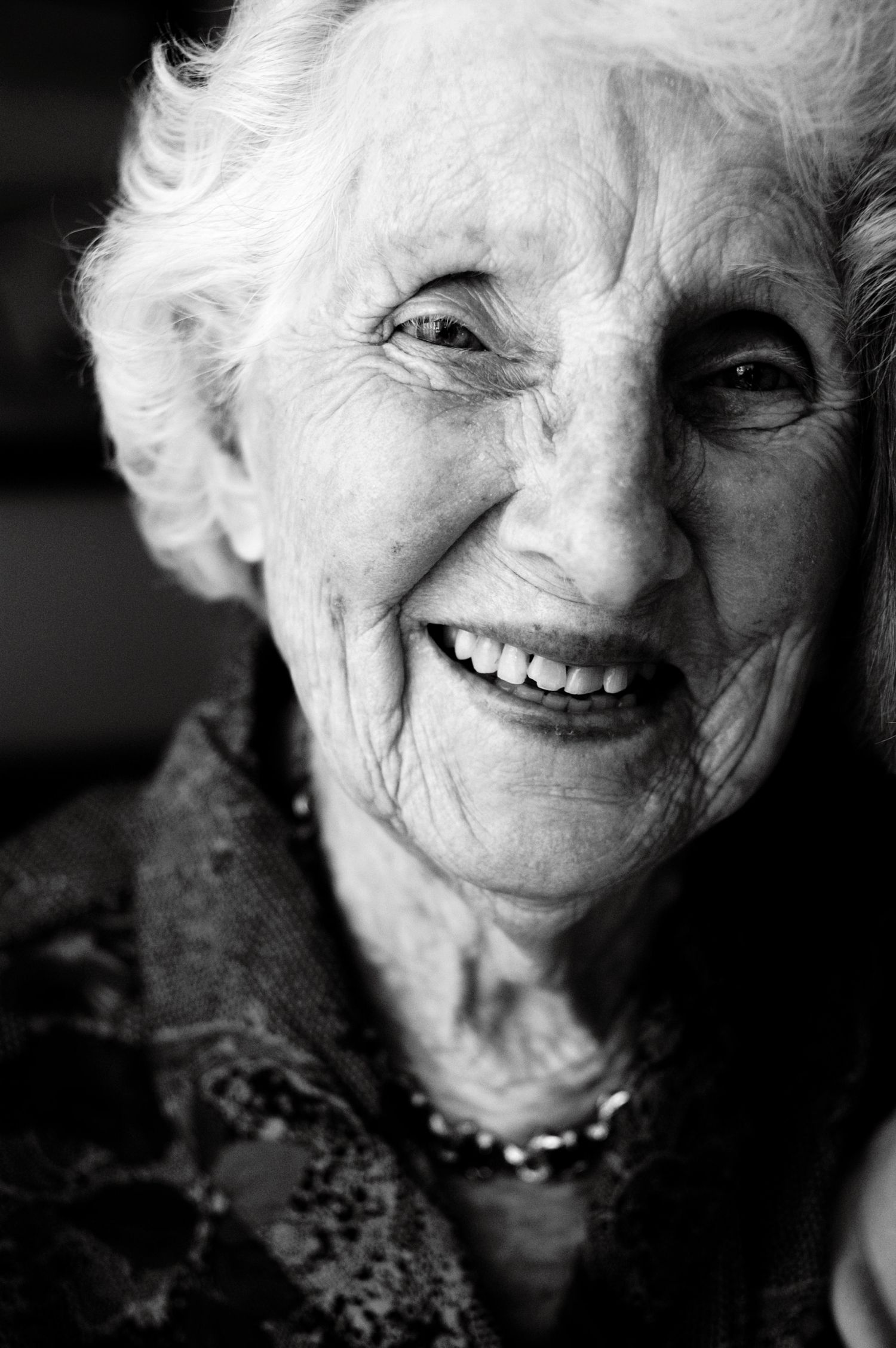 A close-up portrait of an elderly person with white hair smiling warmly in black and white.