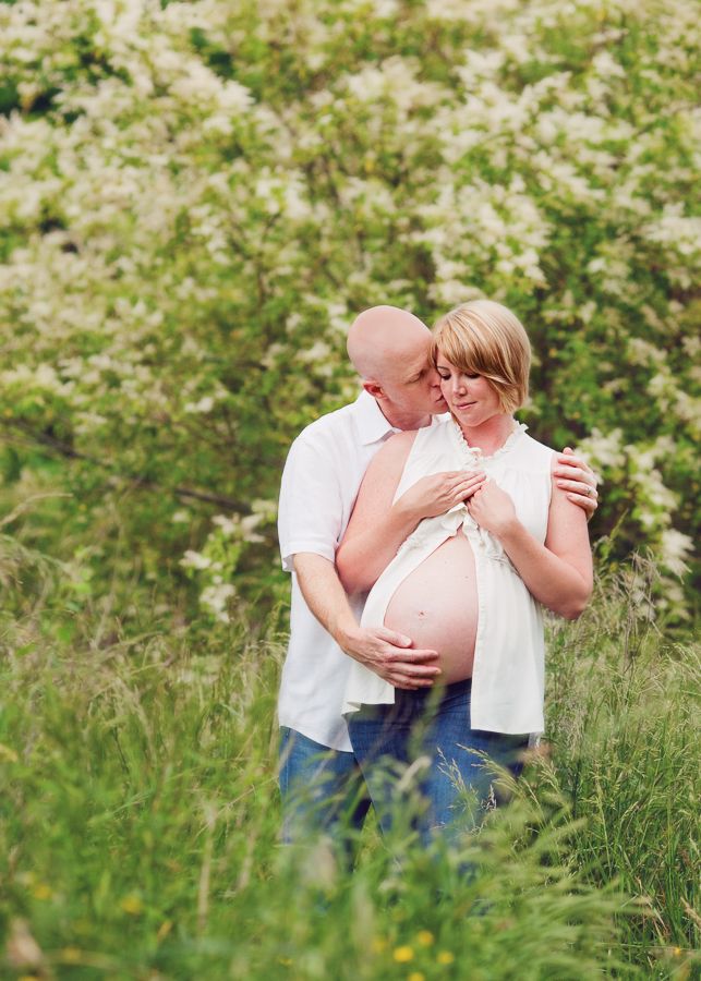 An expectant couple embraces tenderly in a field of wildflowers during a maternity photoshoot.