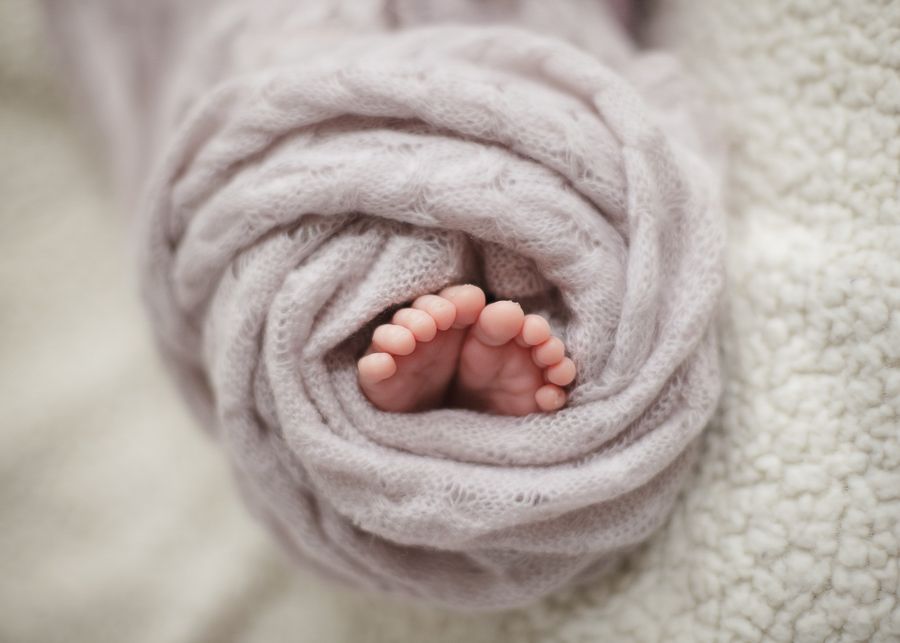 Tiny newborn baby feet wrapped in soft pink blanket.