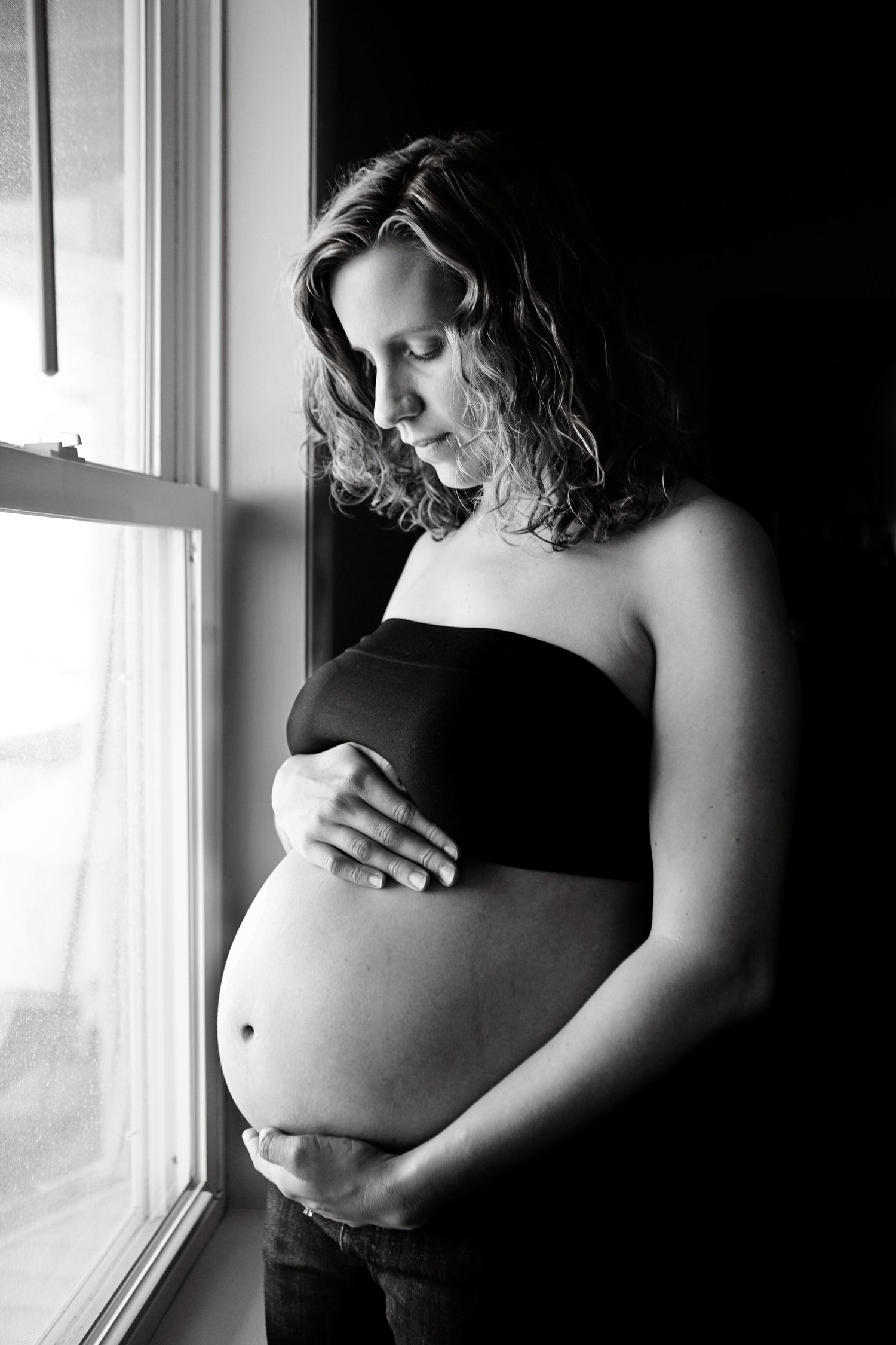 An artistic black and white maternity photo by a window showing an expectant mother.