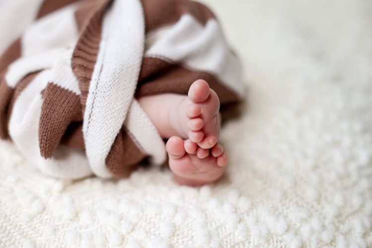 Small baby feet peek out from under a brown and white striped blanket on white fabric.