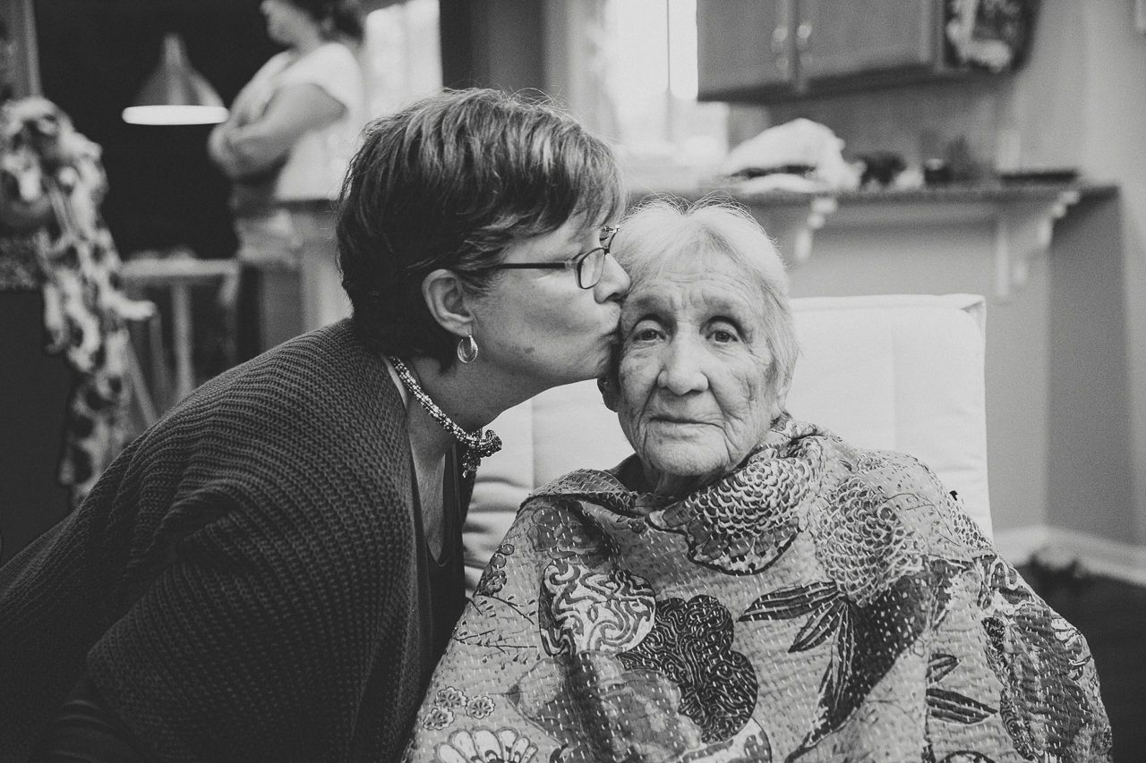 Intimate black and white photo of young person kissing elderly person on cheek.