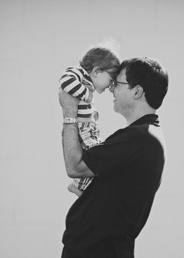 A tender moment between parent and child in black and white as a toddler in stripes is held up high.
