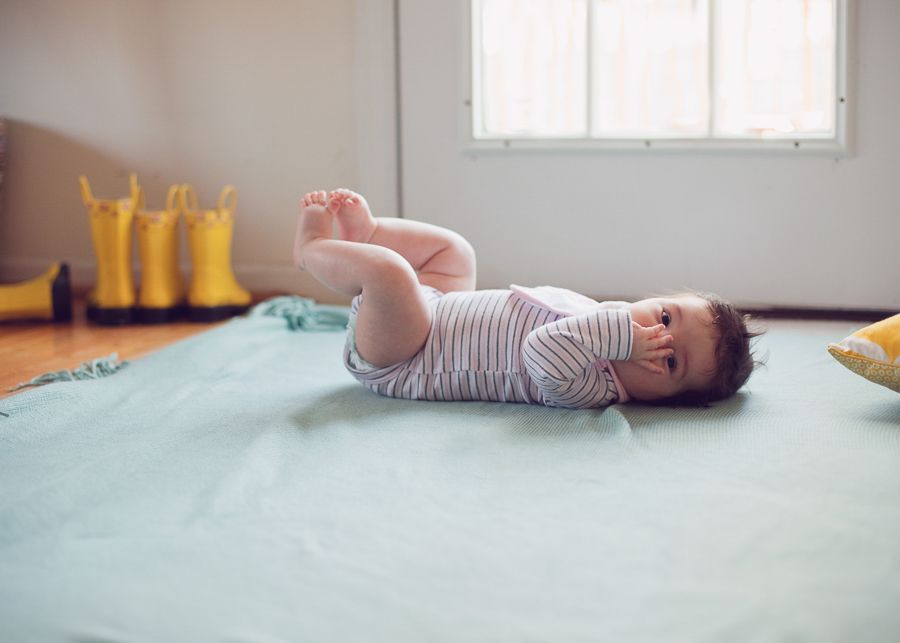 Baby lying on back on mint green surface wearing striped onesie.