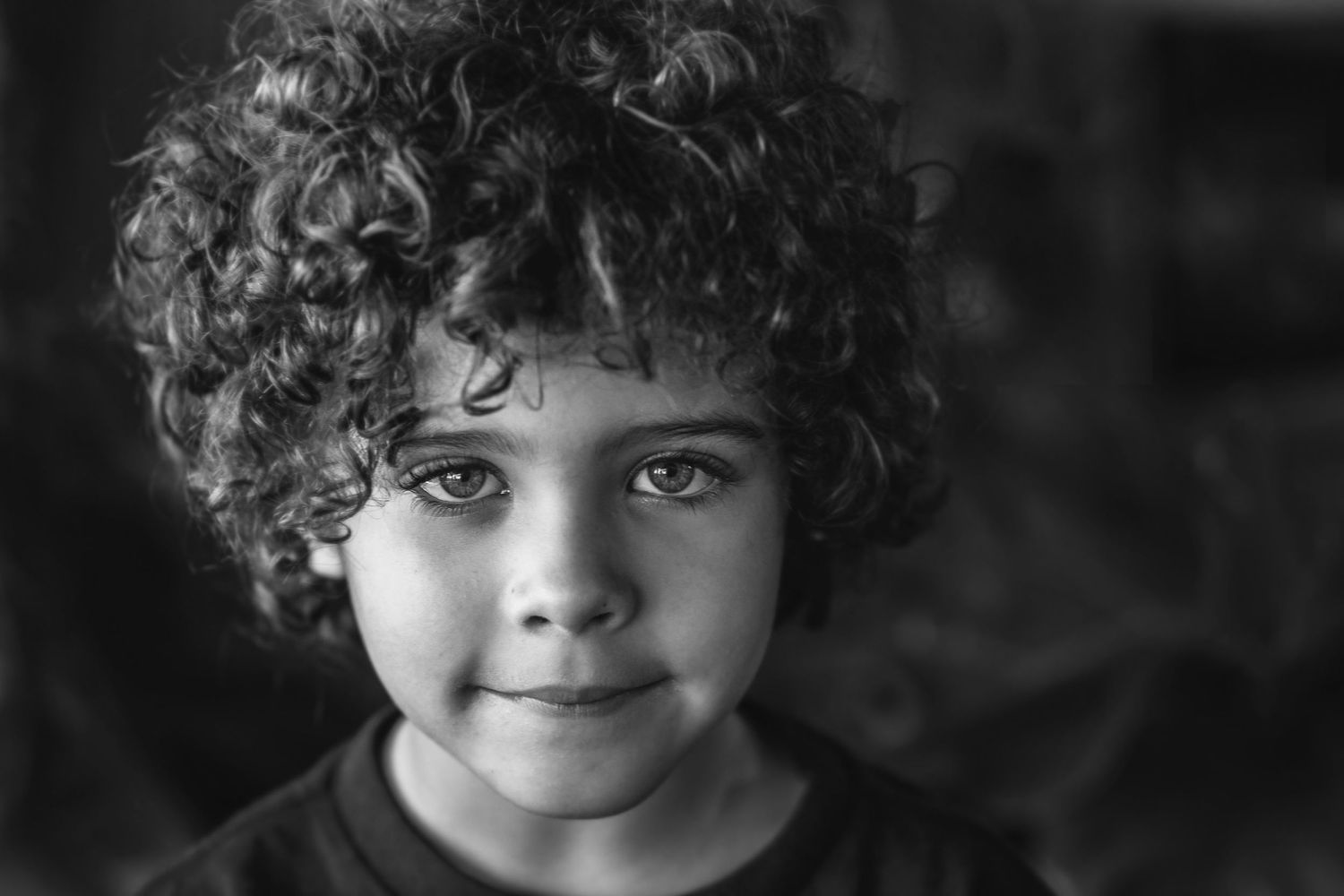 A close-up black and white portrait showcasing natural curly hair and gentle expression.