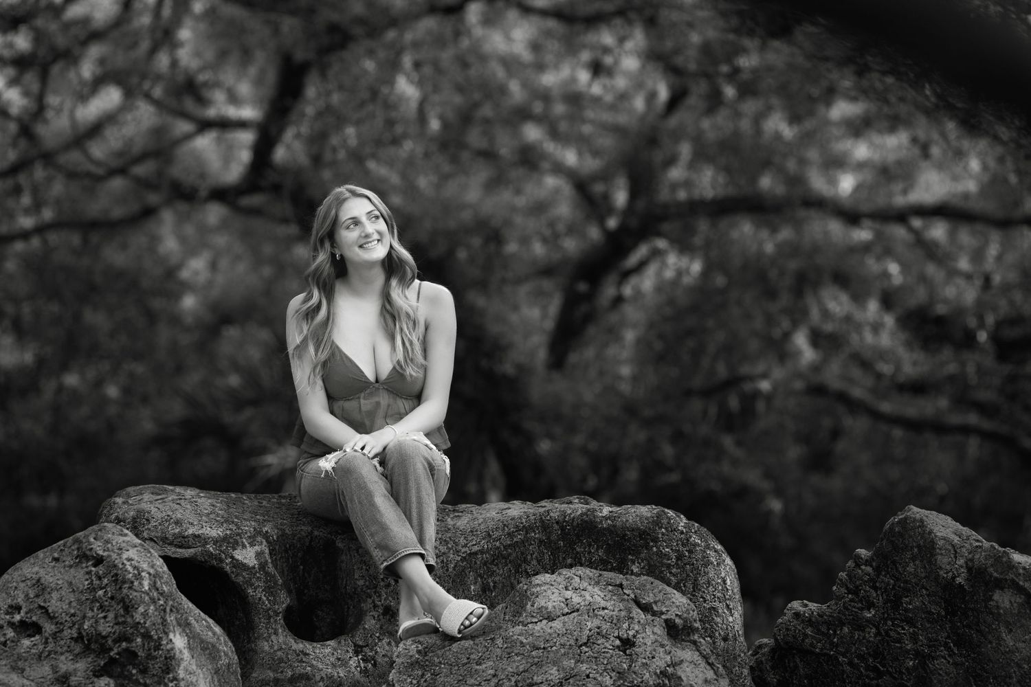 Black and white portrait of someone sitting thoughtfully on rocky terrain.