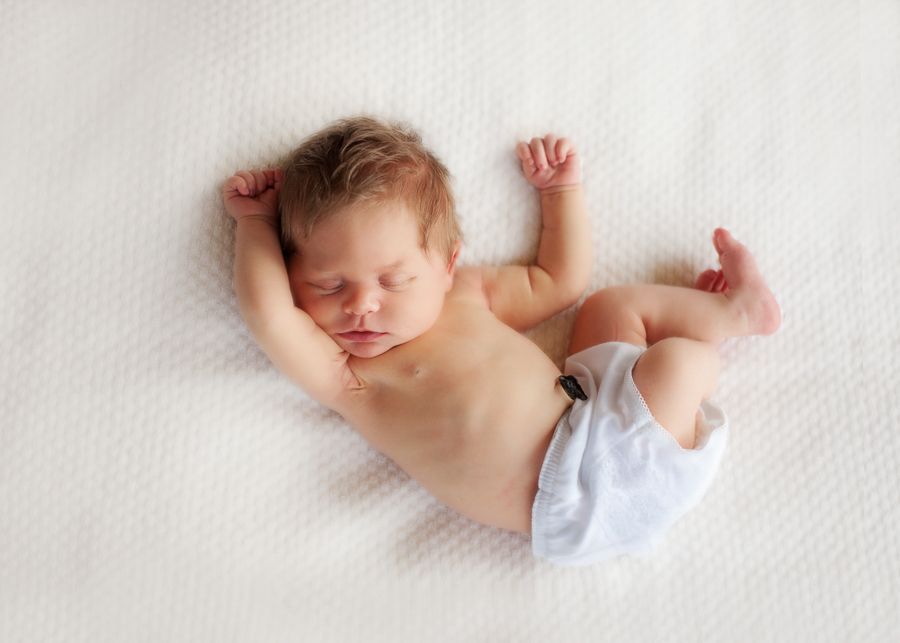 Sleeping newborn baby stretching on white textured blanket.