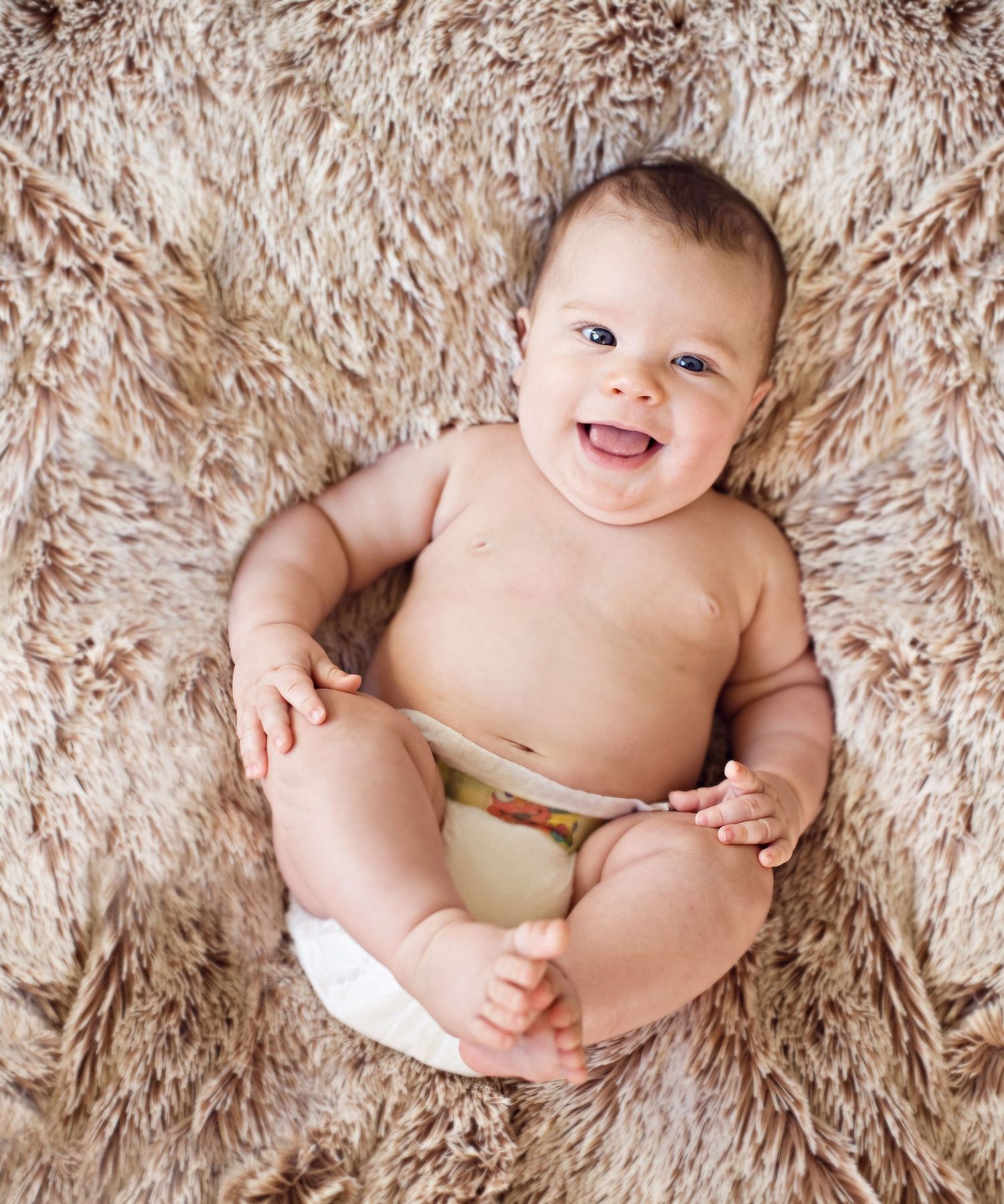 A happy baby wearing a diaper lying on fluffy beige carpet.