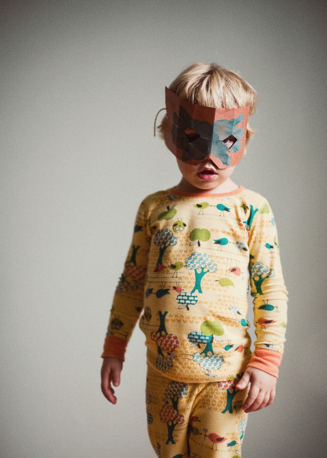 Young child wearing colorful patterned pajamas and face paint against grey background.