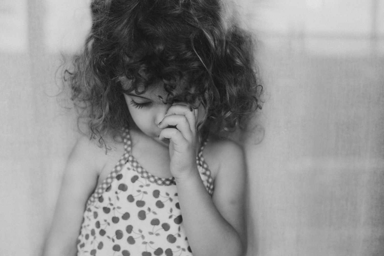 An expressive black and white portrait of a curly-haired child in a polka dot dress.