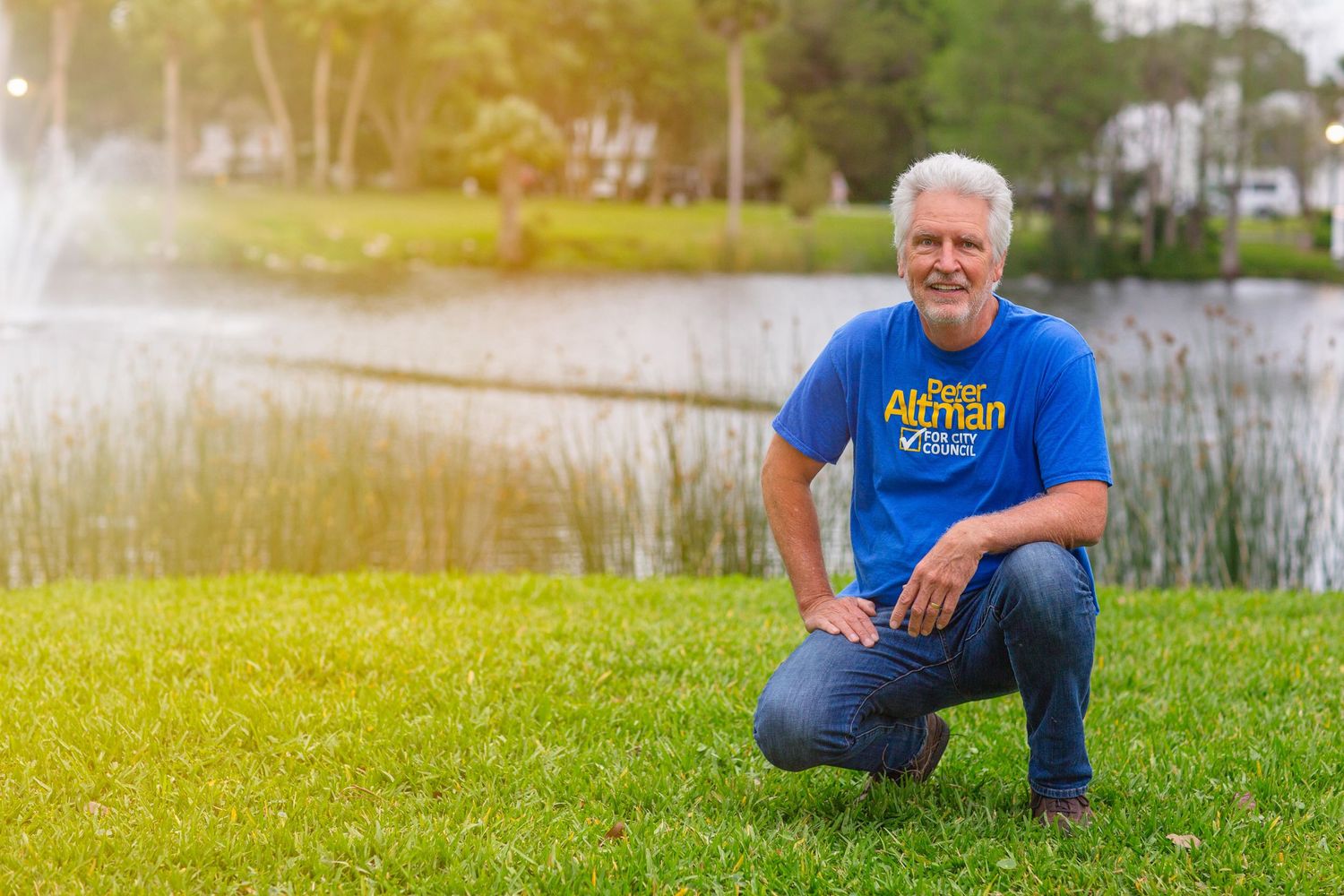 Person in blue t-shirt kneeling by a serene lake on a sunny day.