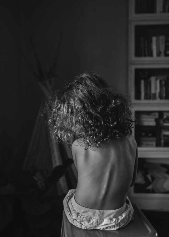 Black and white image showing the bare back of someone with curly hair.