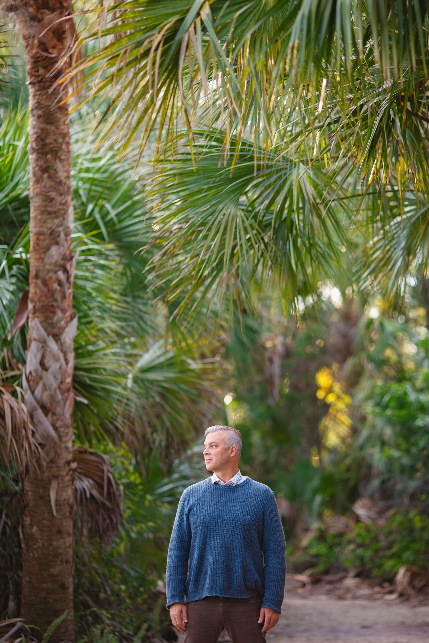 Person in blue sweater standing among tropical palm trees.