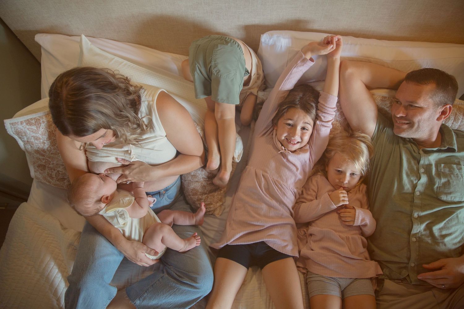 Happy family relaxing together on a bed, parents with young children laughing and playing in a cozy bedroom.