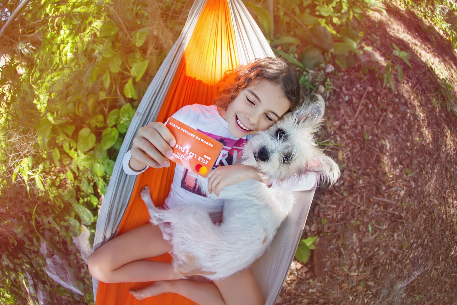 A relaxing moment in an orange hammock with a small white dog on a sunny day.