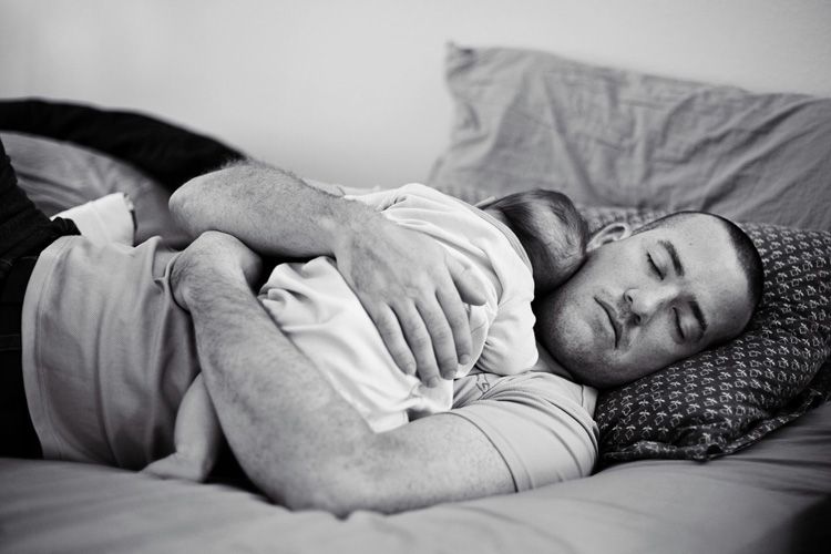 Person sleeping peacefully in bed while holding a baby close to their chest.