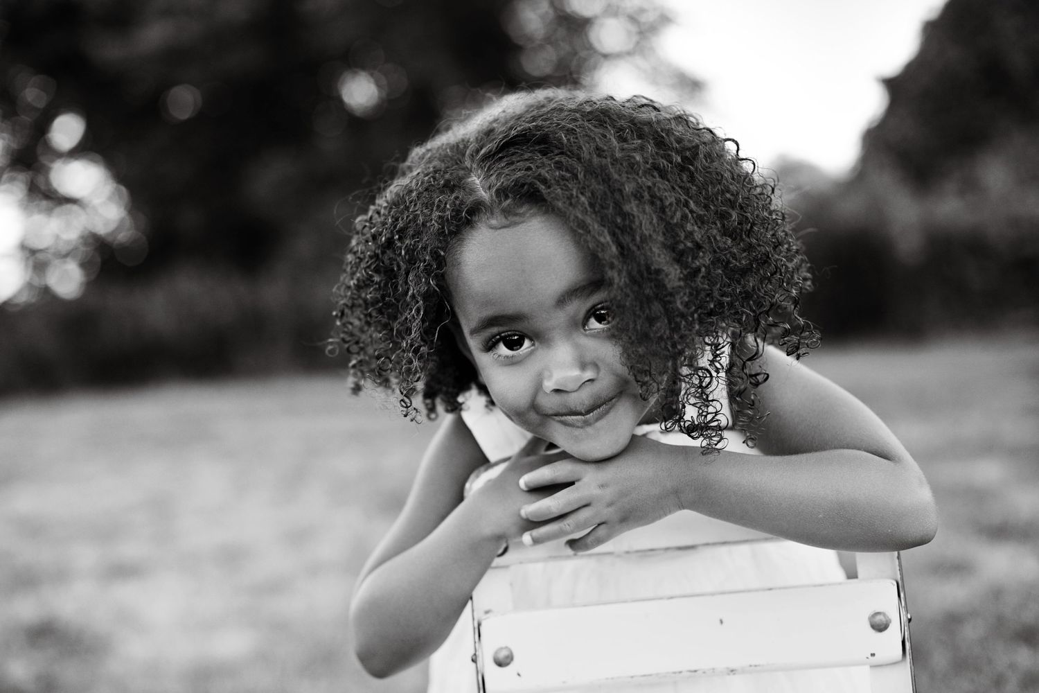 A joyful portrait of a child with curly hair leaning on a white surface outdoors.