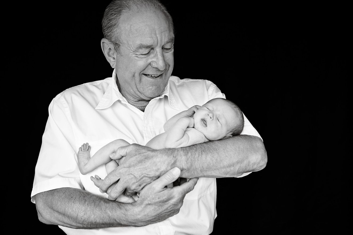 An elderly person in white clothing holds a sleeping newborn baby against a dark background.