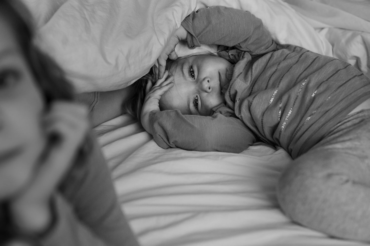 Black and white intimate portrait of someone lying peacefully on white bedding.