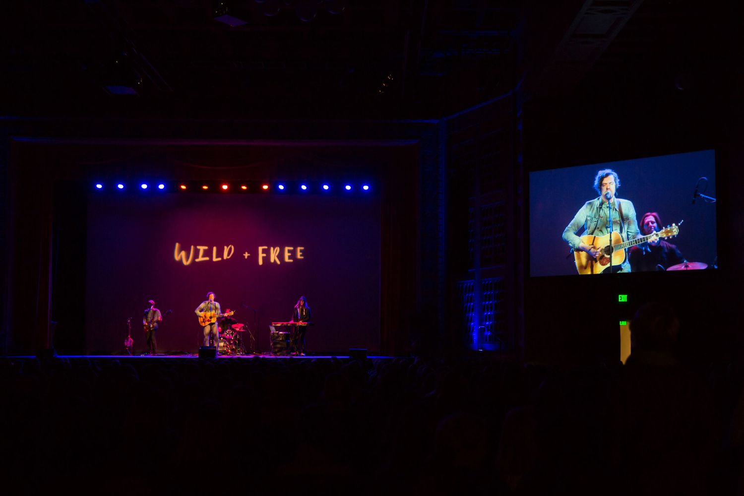 Concert stage with performers and video screen displaying live music performance.