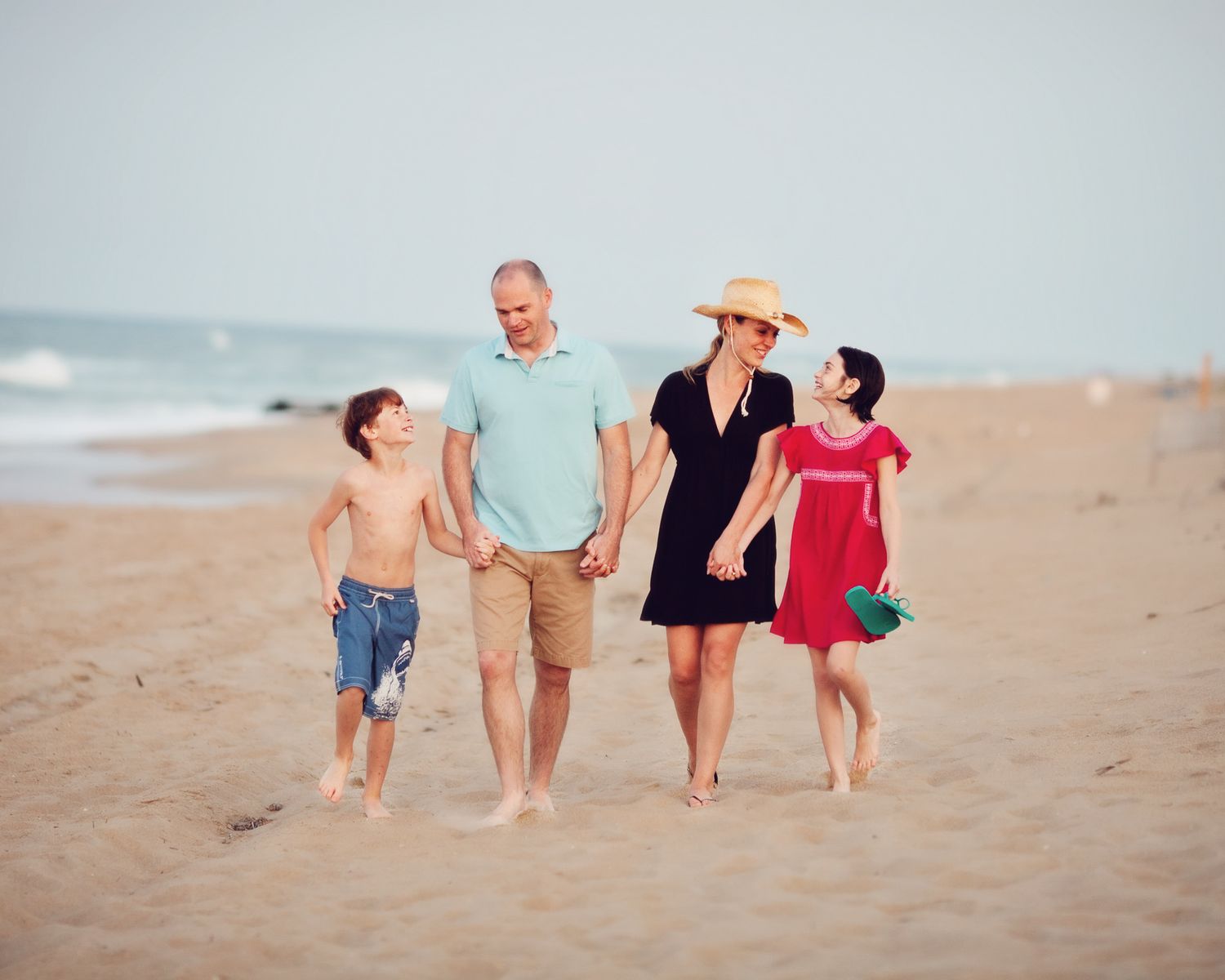 Family walking together along a sandy beach at sunset with ocean waves in background.