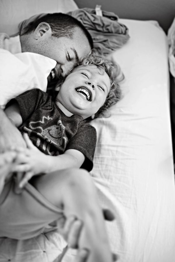 Black and white candid photo of two children laughing and playing on a bed.