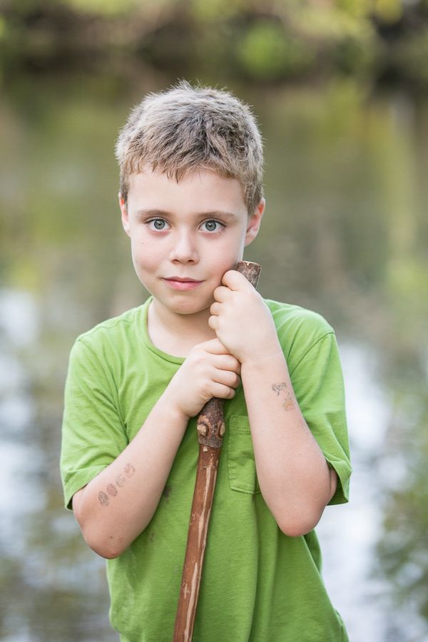 Youth in green t-shirt holding wooden stick by water.