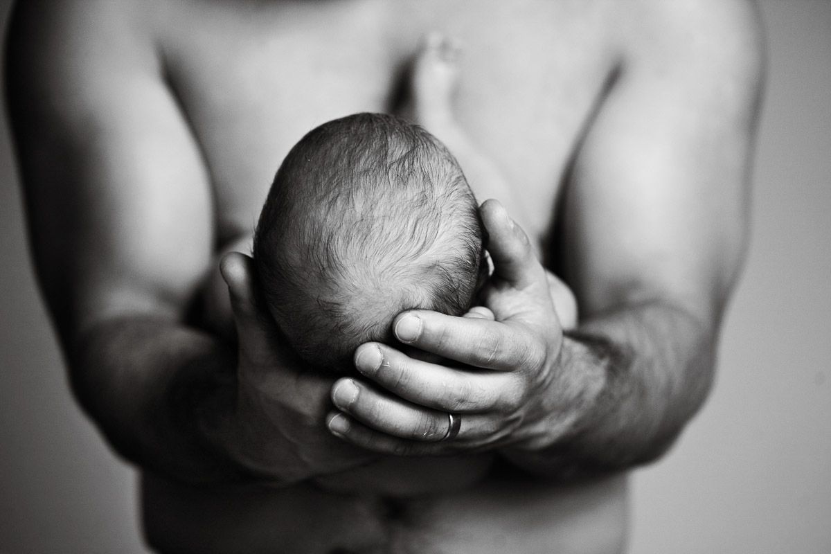 Black and white artistic photo showing gentle hands cradling a newborn.