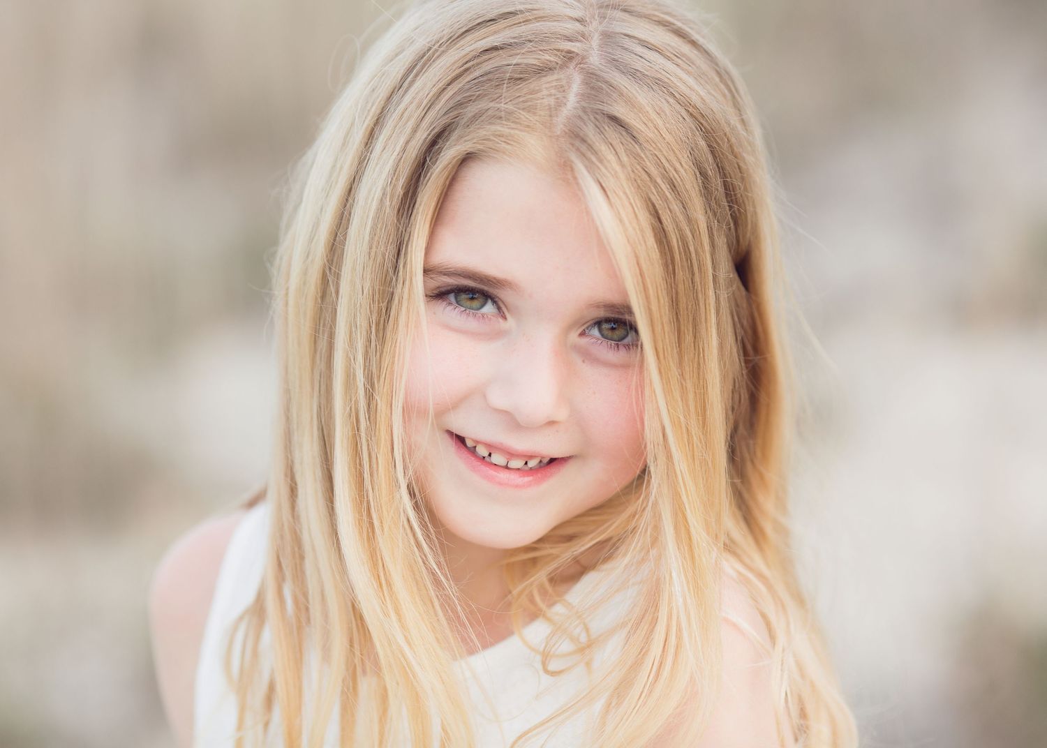 Portrait of a smiling young person with long blonde hair against a soft blurred background.