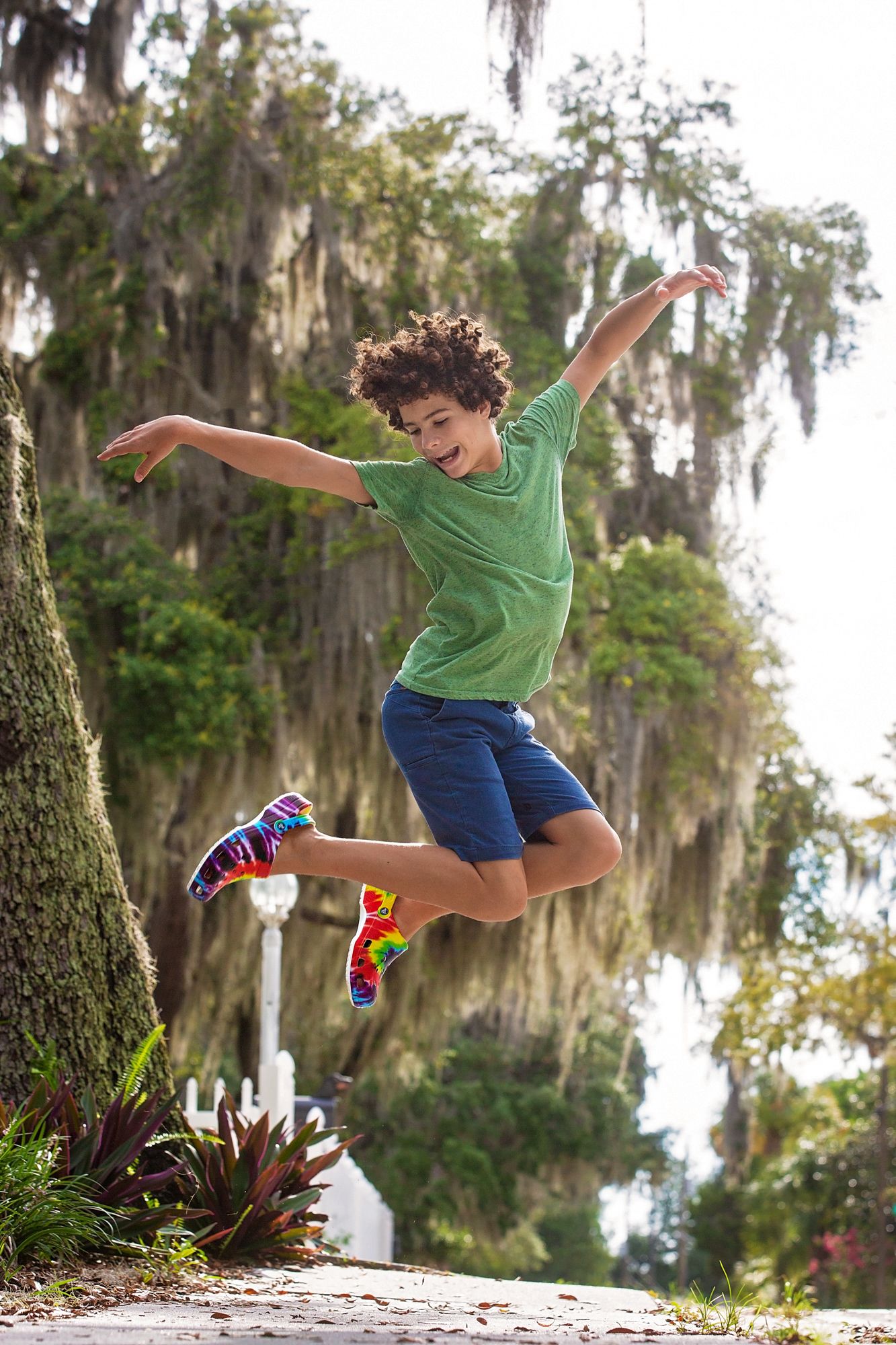 A joyful leap captured mid-air among Spanish moss-draped trees in a garden setting.