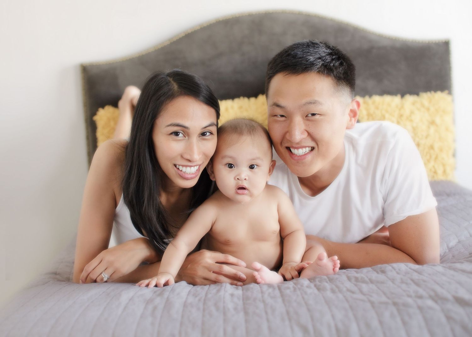 Happy family relaxing together on gray bed with yellow pillows.