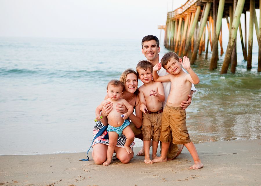 Happy family group sitting together on beach with pier in background during sunset.