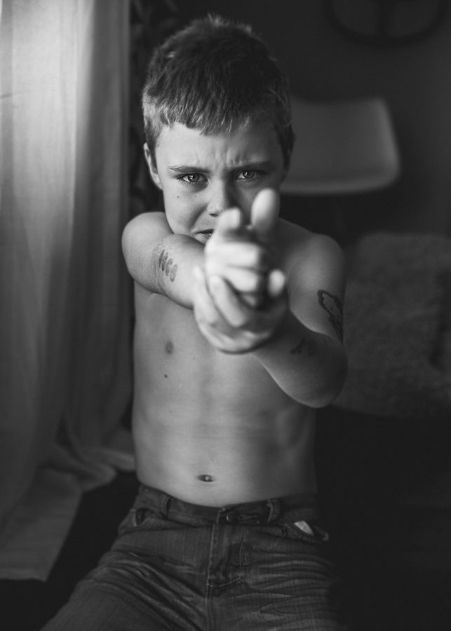 Black and white image of a shirtless child pointing forward with intense expression.