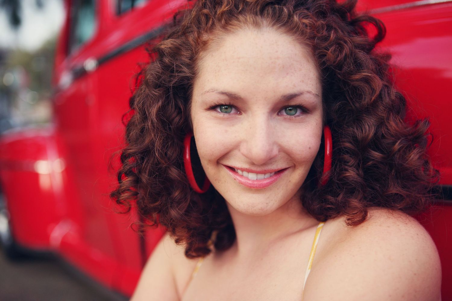 Natural portrait with curly red hair against red vehicle background.