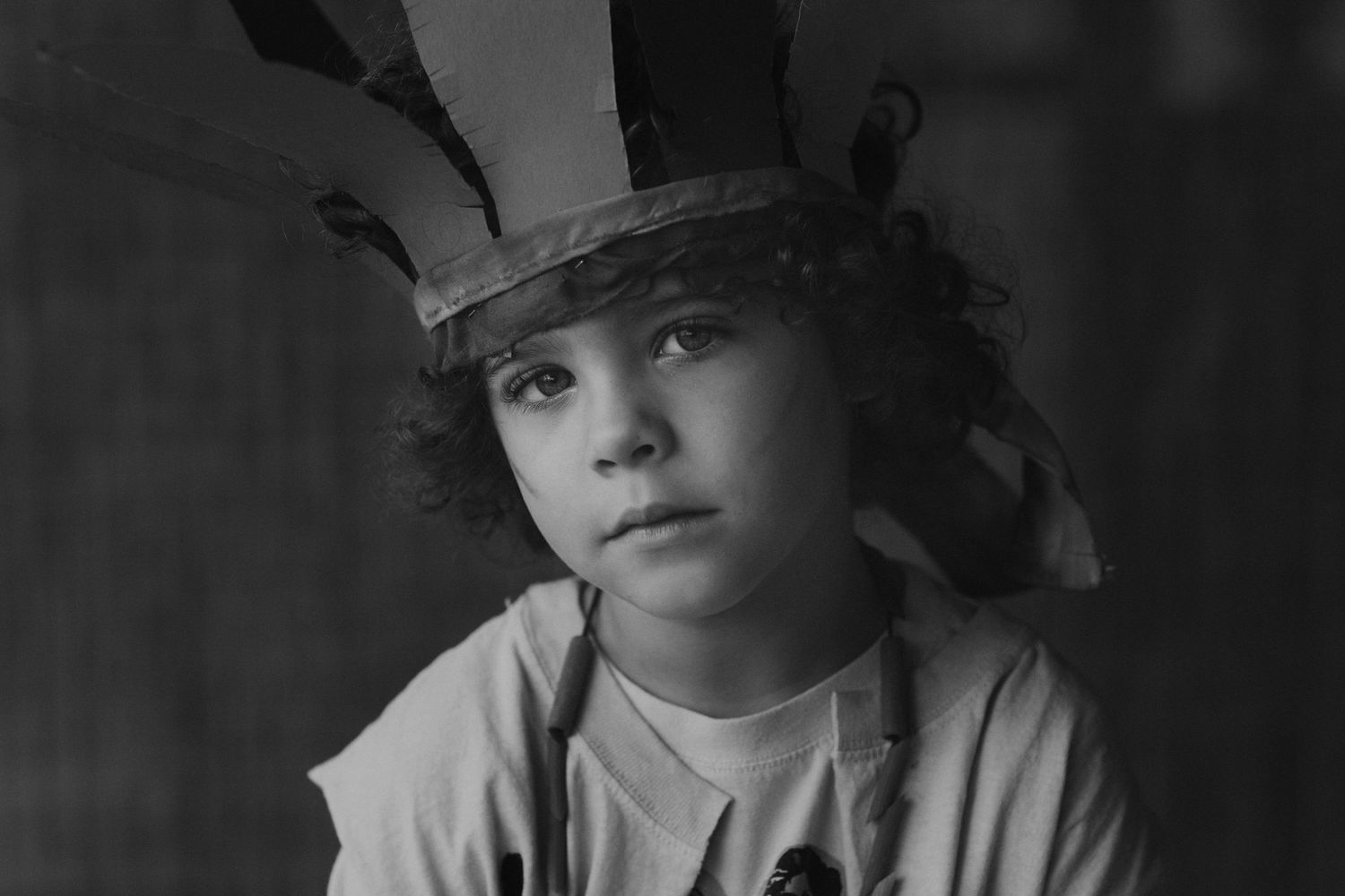 Moody black and white portrait of young person wearing handmade paper crown.