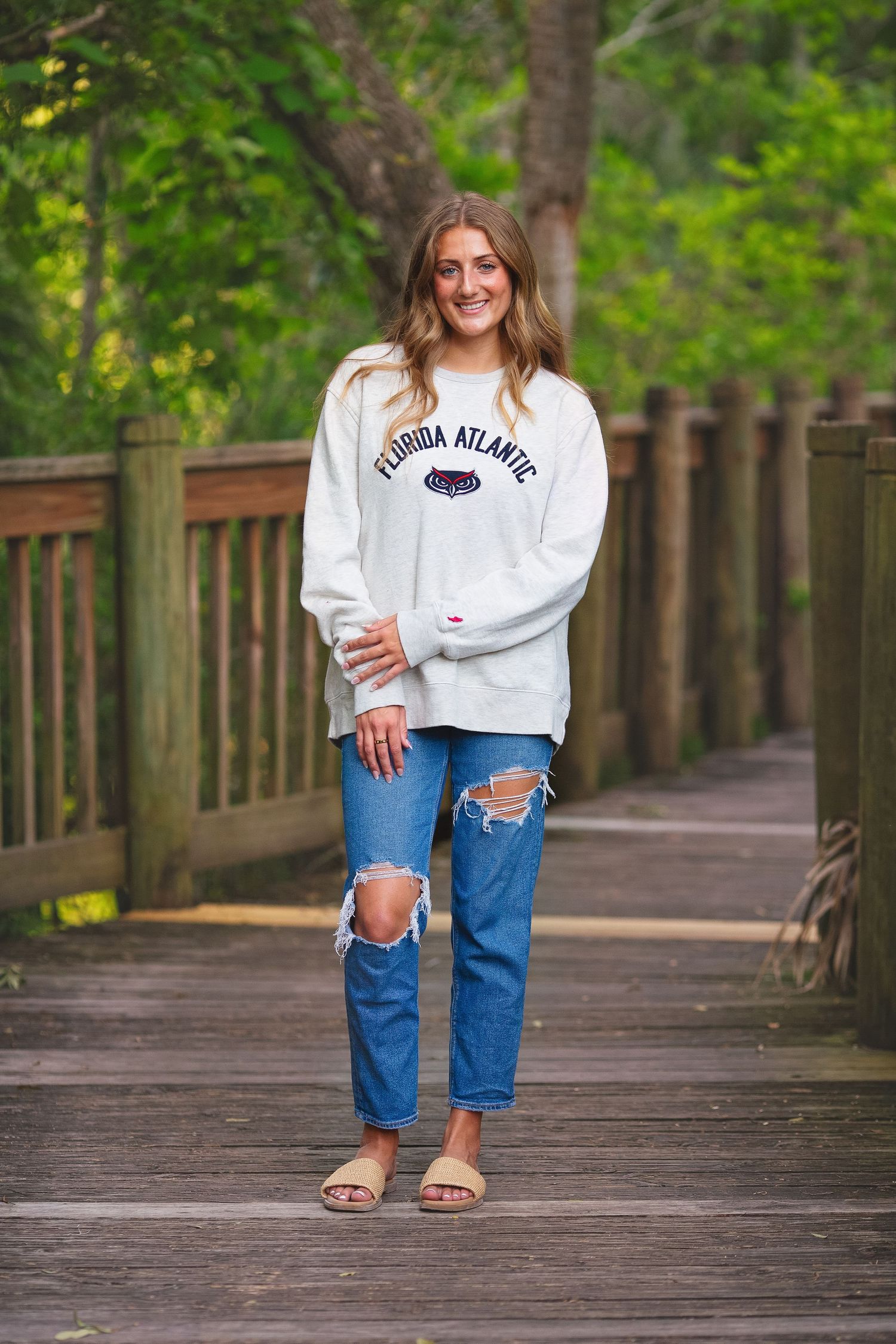 Person in distressed jeans and college sweatshirt standing on wooden boardwalk.