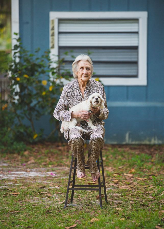 Senior woman sitting on tall stool outdoors holding small dog.