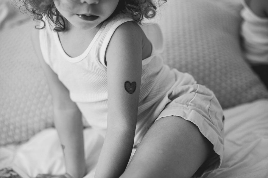Close-up black and white image showing a small heart tattoo on a child's arm.