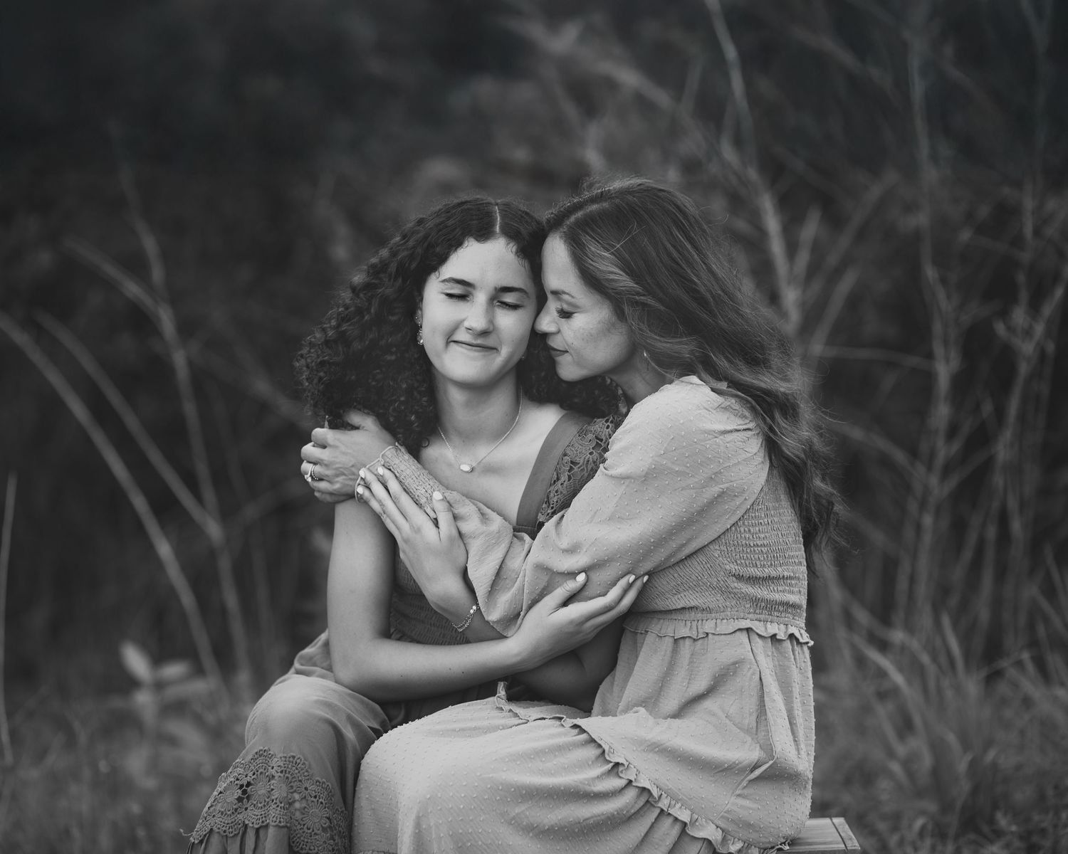 Black and white photo of two young women embracing outdoors, one kissing the others cheek affectionately.