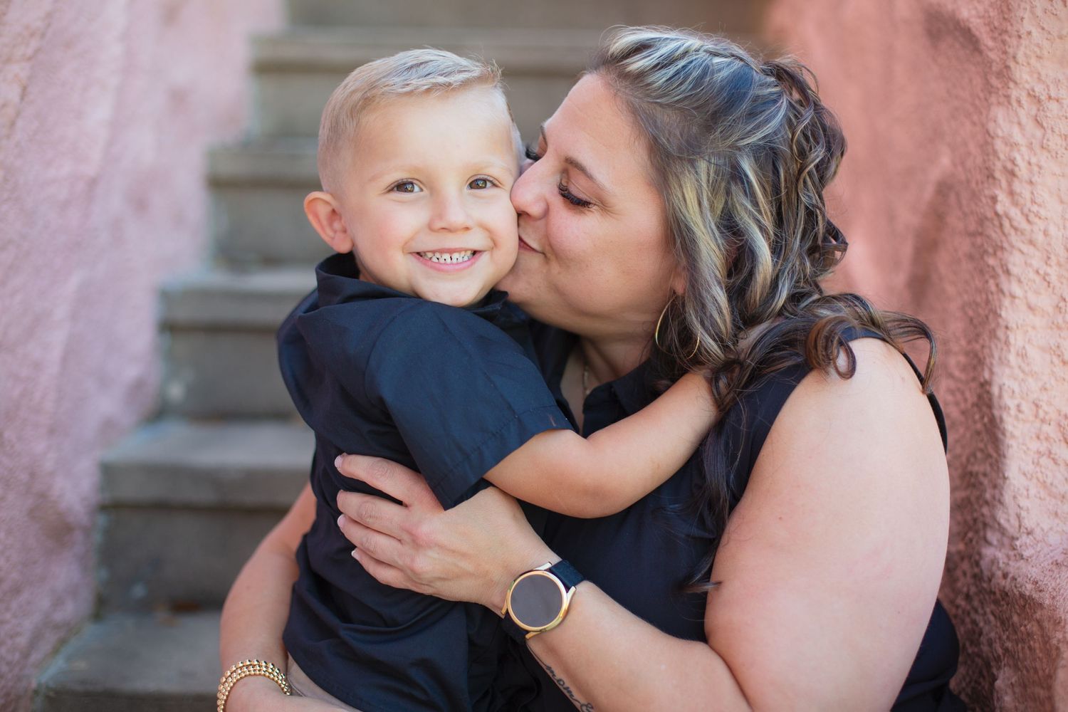 A tender moment captured between a mother and young child on stone steps against a pink wall.