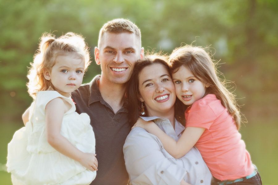 Happy family of four posing together outdoors in natural lighting.