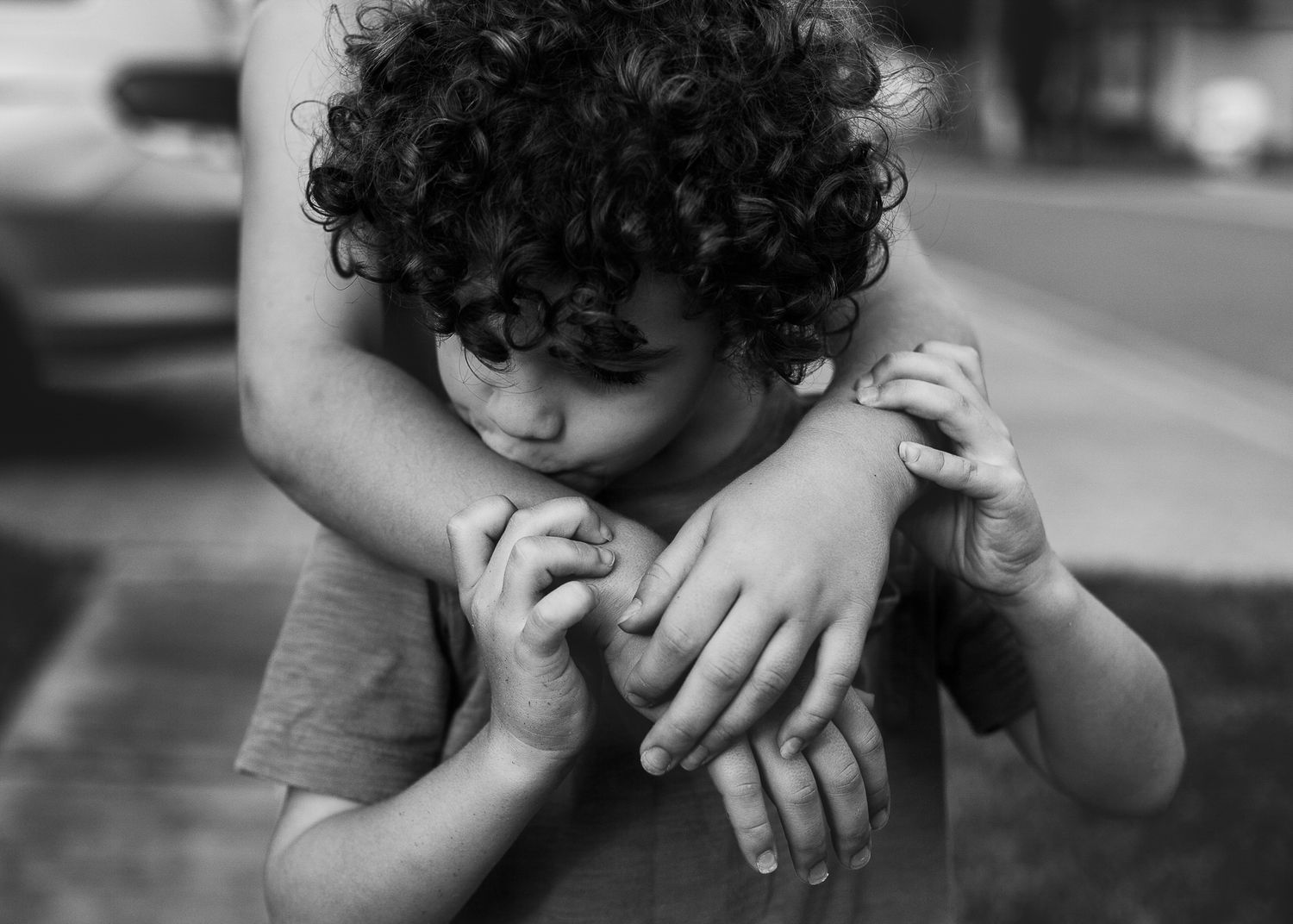 Black and white image of a child with curly hair being comforted by adult hands.