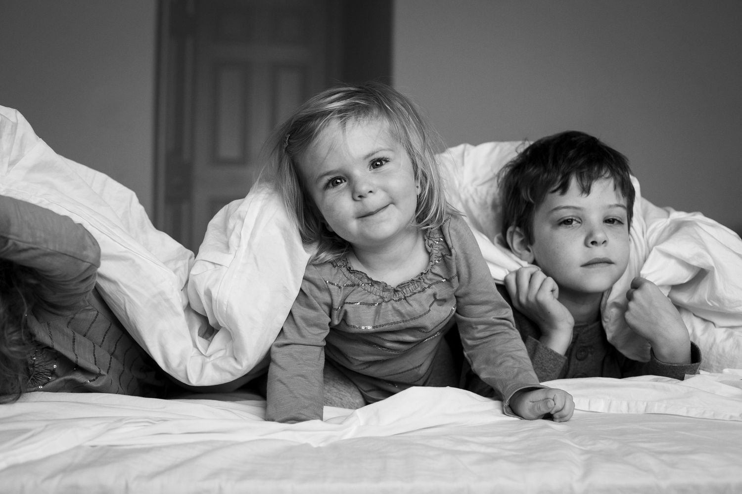 Black and white portrait of children laying on bed with playful expressions.