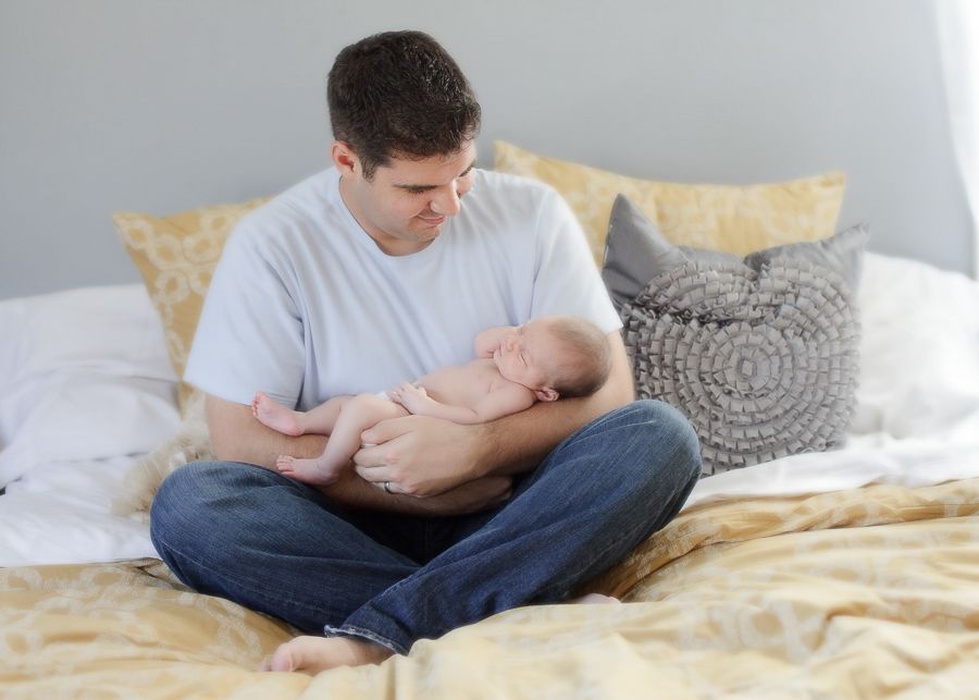Gentle parental bonding moment with infant on comfortable bed with decorative pillows.