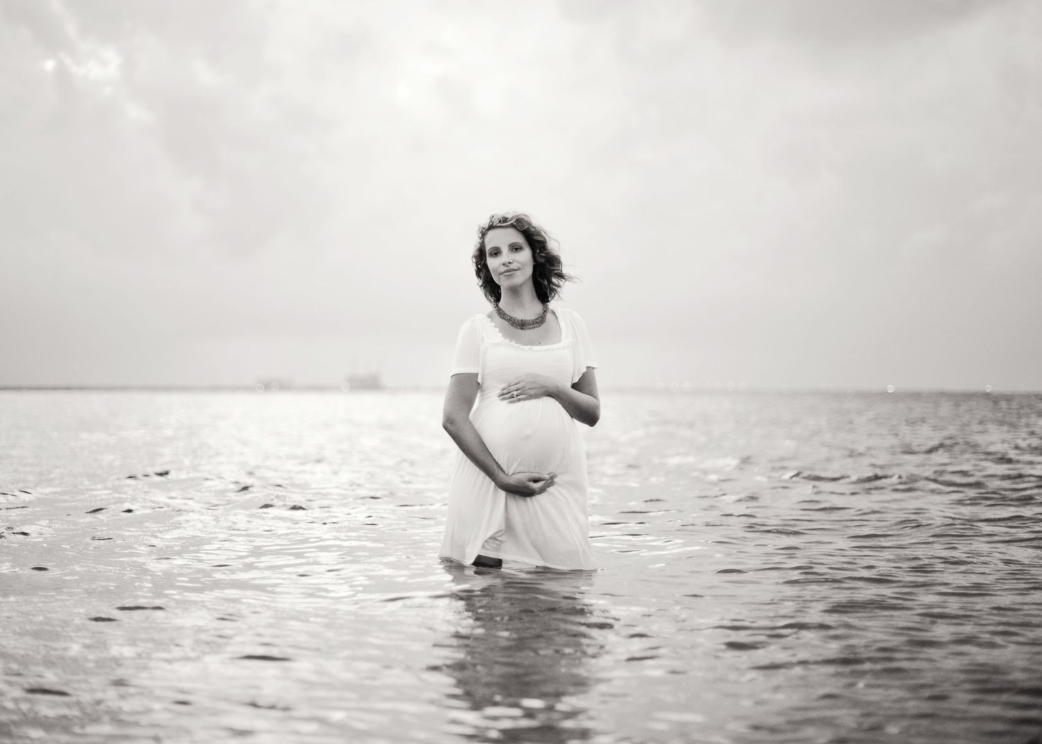 Vintage style photo of person standing in shallow ocean water while wearing white dress.