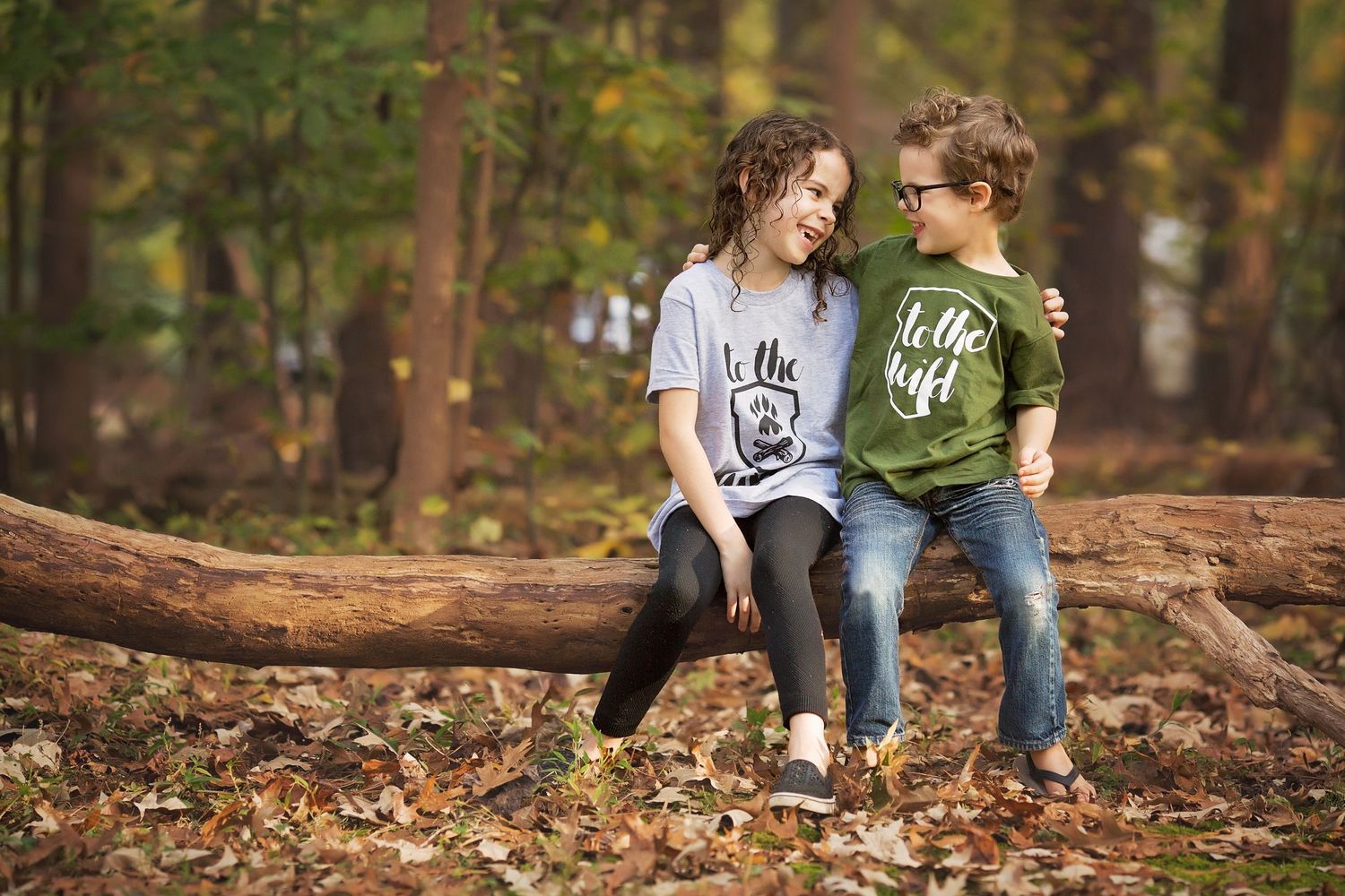 Two people sitting on fallen log in autumn forest.